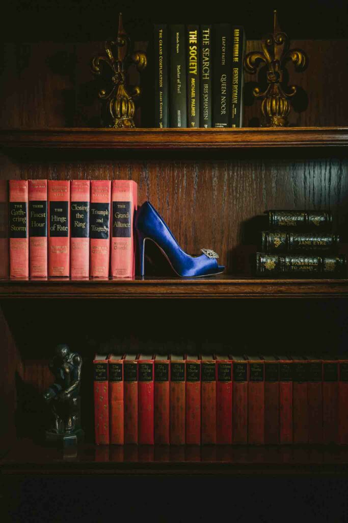 A blue wedding shoe on a book shelf with old hard cover books.