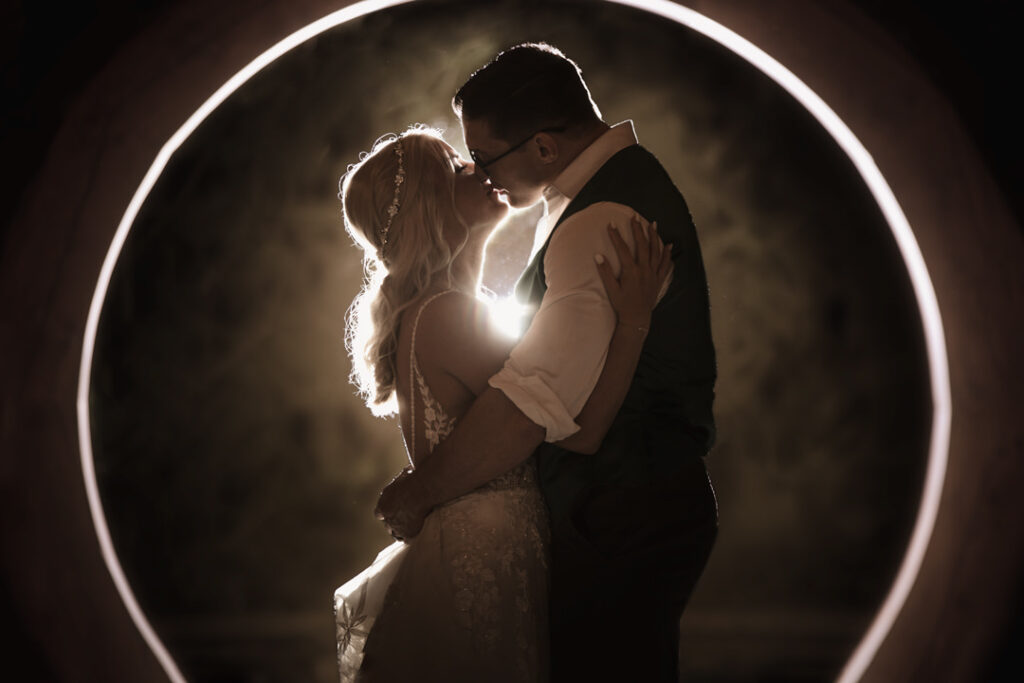 A creative colorado wedding photo with a couple kissing with a lit up circle behind them.