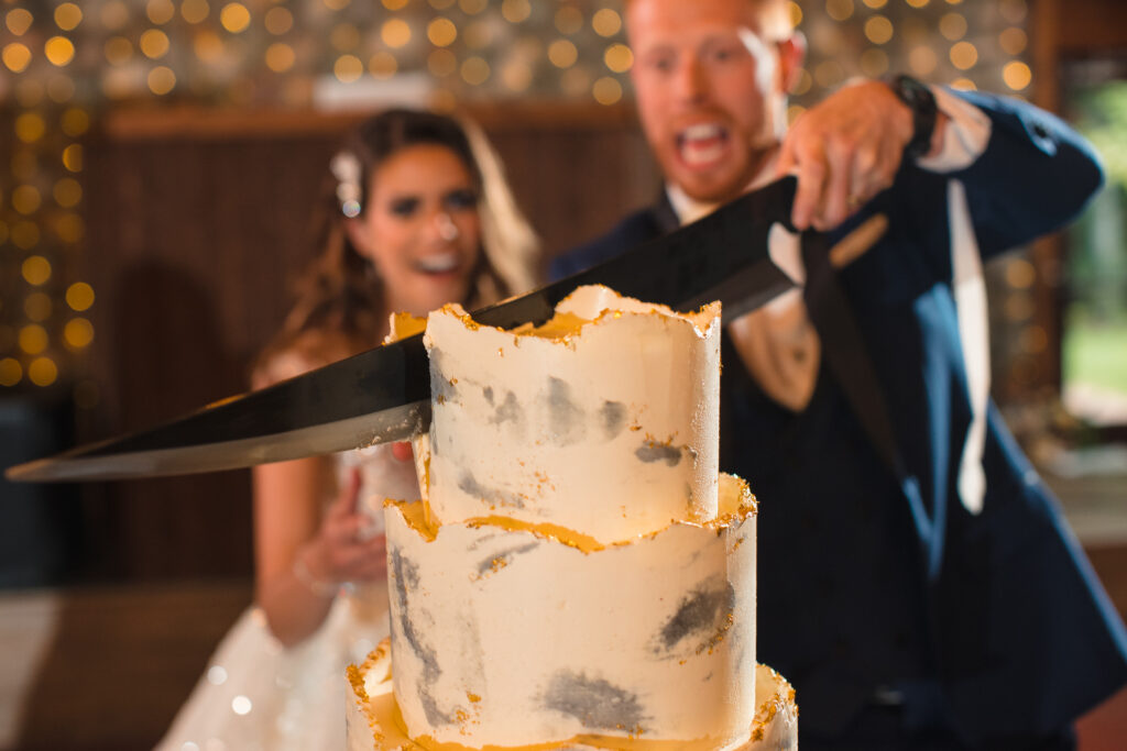 A bride and groom cut their wedding cake with a giant sword.
